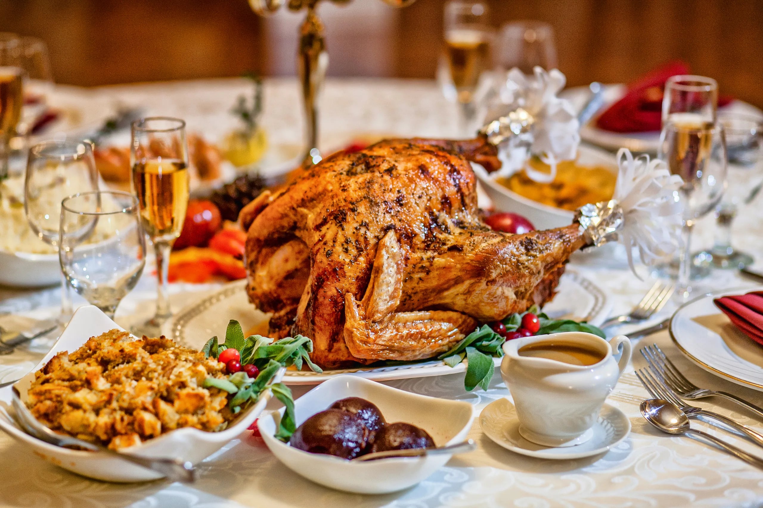 A roasted Thanksgiving turkey on a set table with stuffing, cranberry sauce, and gravy